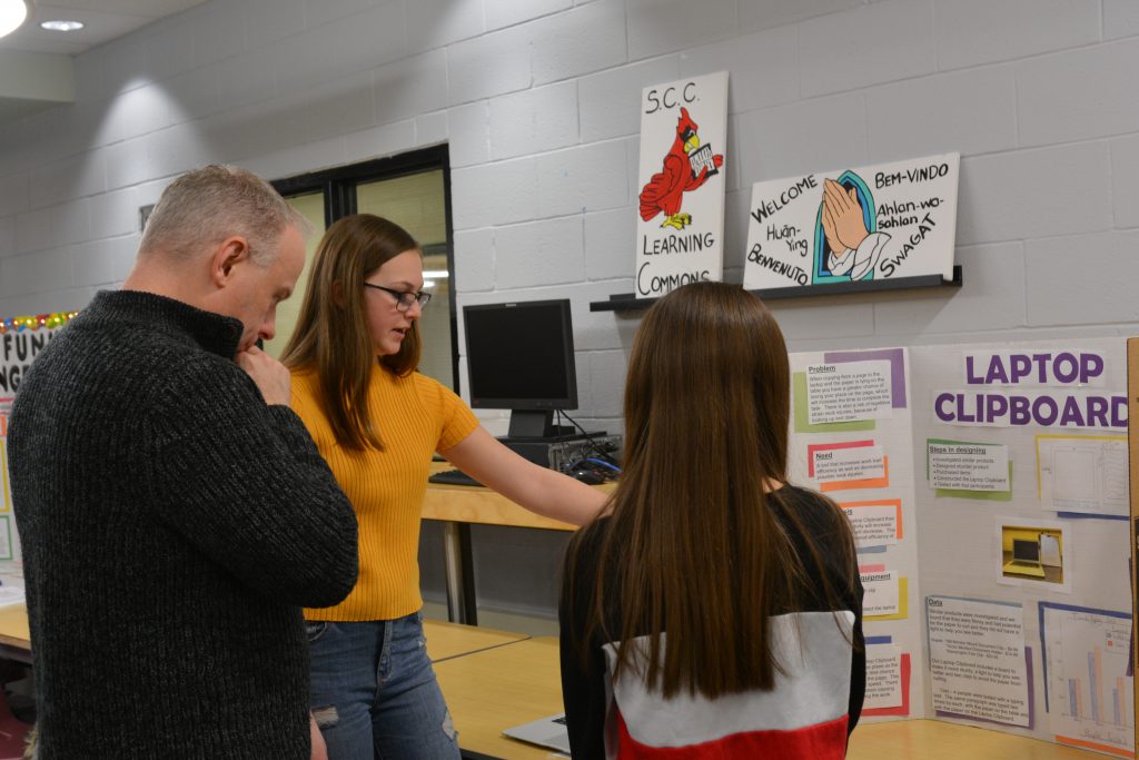 A judge asks two female students questions about their project. 