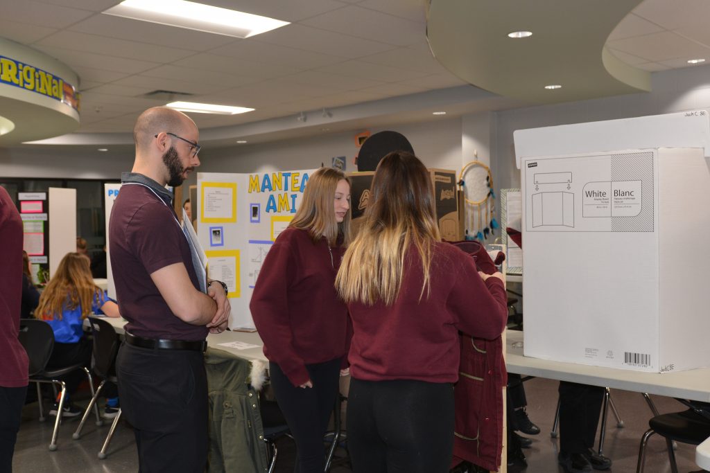 A judge watches as two female students demonstrate their project. 