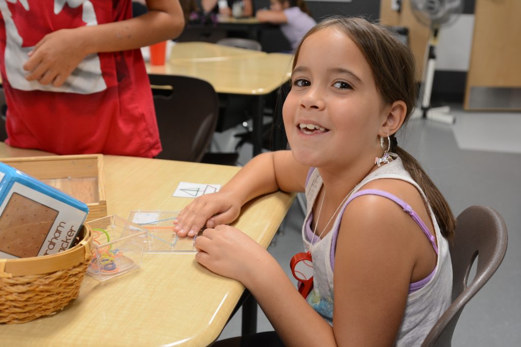 A student is all smiles as she completes a shape building activity with elastics.