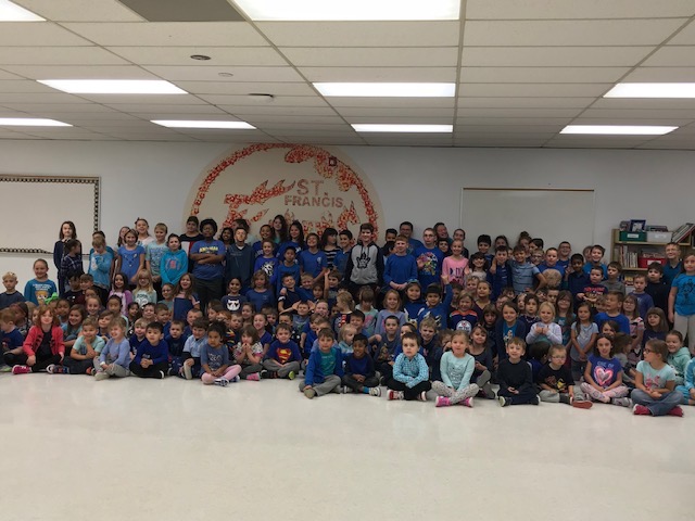 Group of students and staff members from St. Francis school dressed in blue sit smiling.