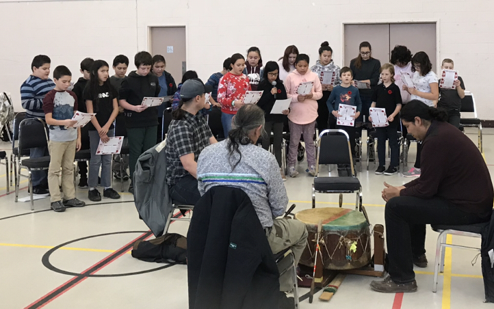 Students sing O'Canada as traditional Indigenous drumming takes place in the centre
