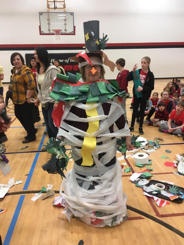 A giant crafted snowman stands in the centre of the school gym, with student and staff surrounding it and laughing.
