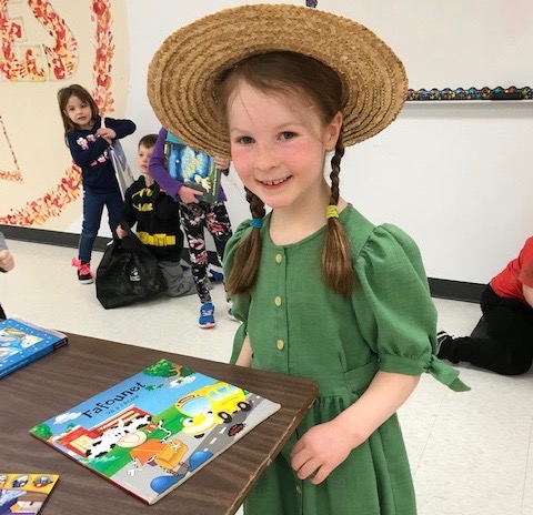 A girl smiles as she points to her book.