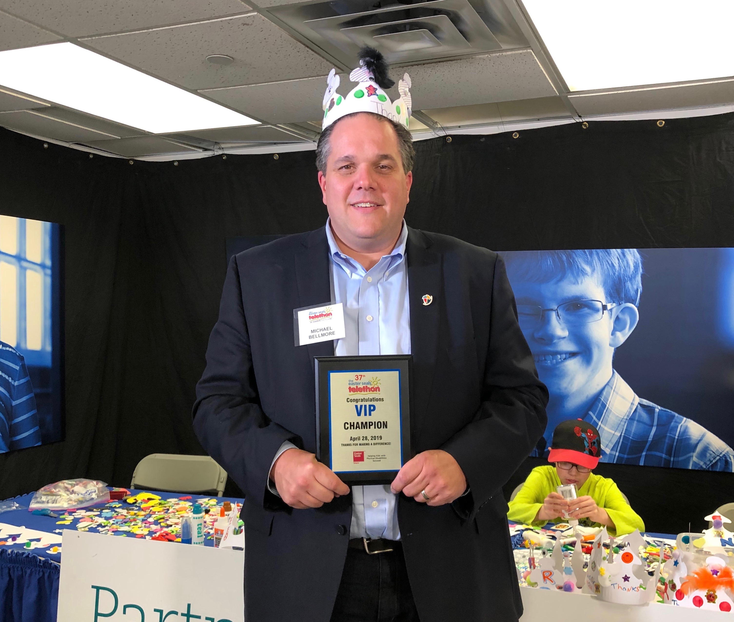 Board Chair Michael Bellmore stands with his VIP Champion Plaque