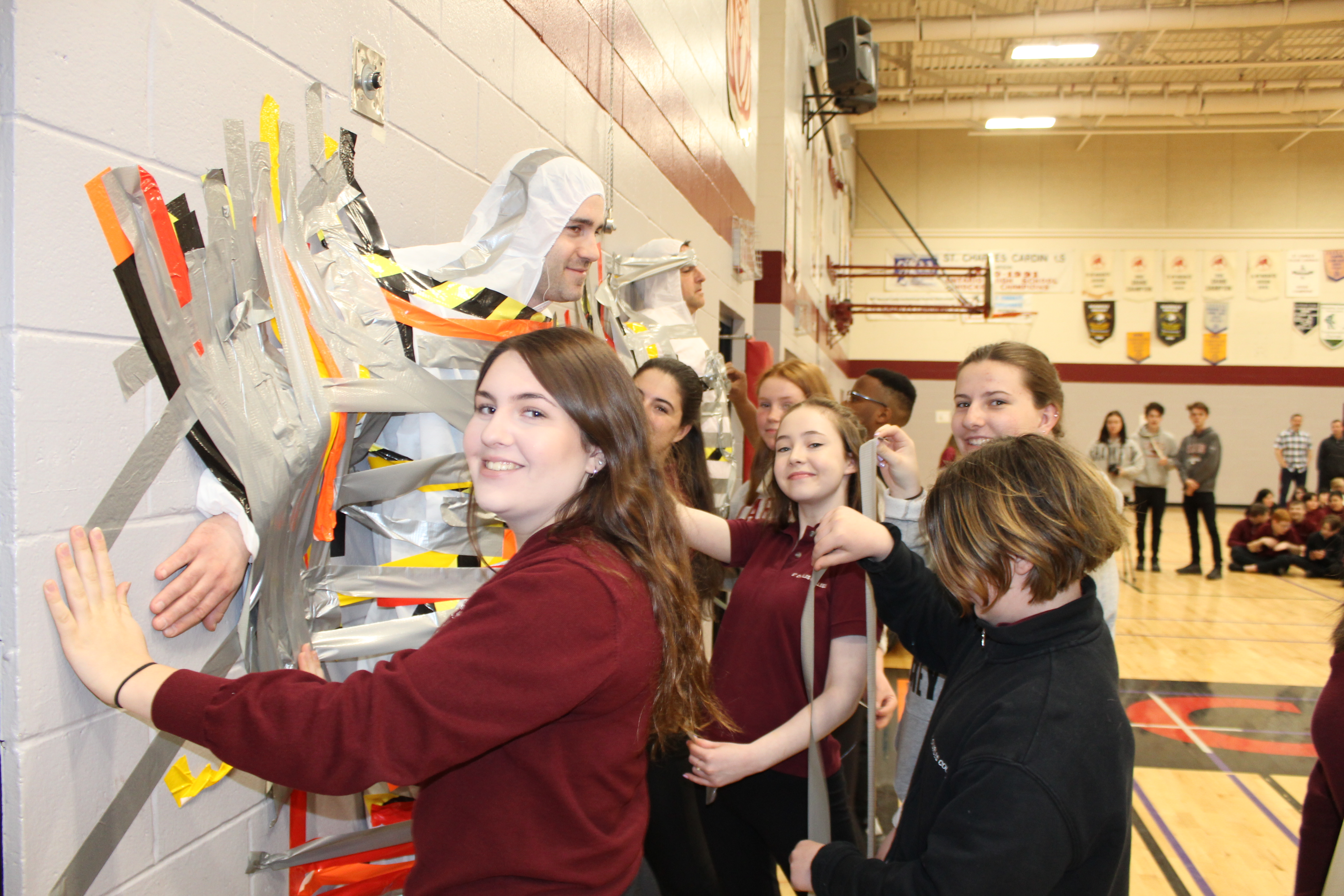 A group of girls tape their Vice Principal to the wall.