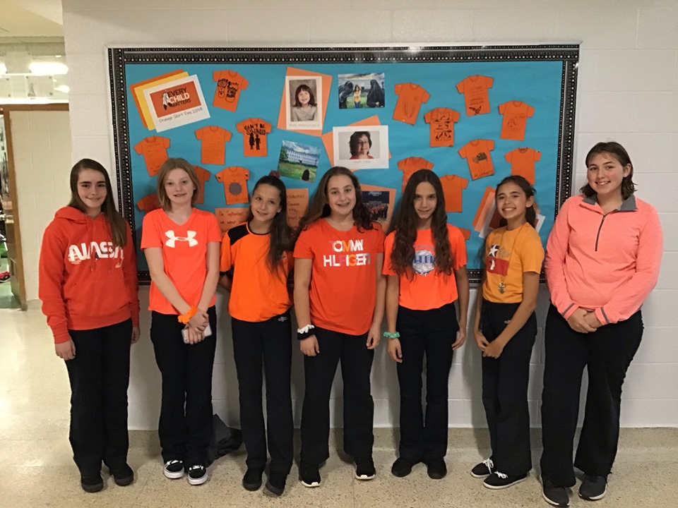 A group of girls wear their orange shirts and stand in a line.