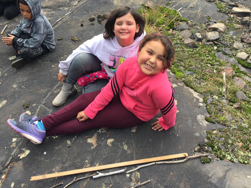 Two girls lay next to a stick used for measurement.