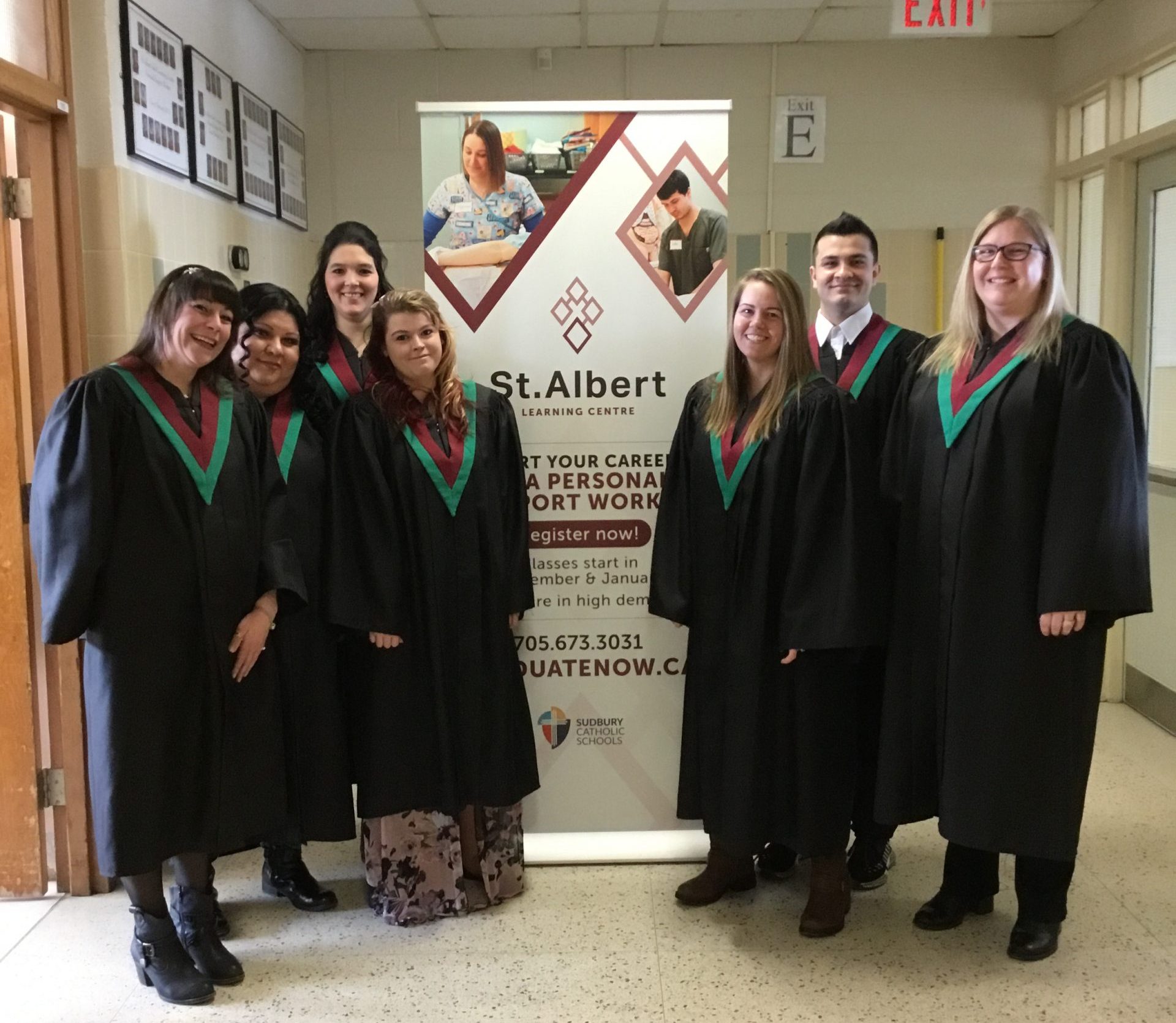 Grads stand next to the program banner.