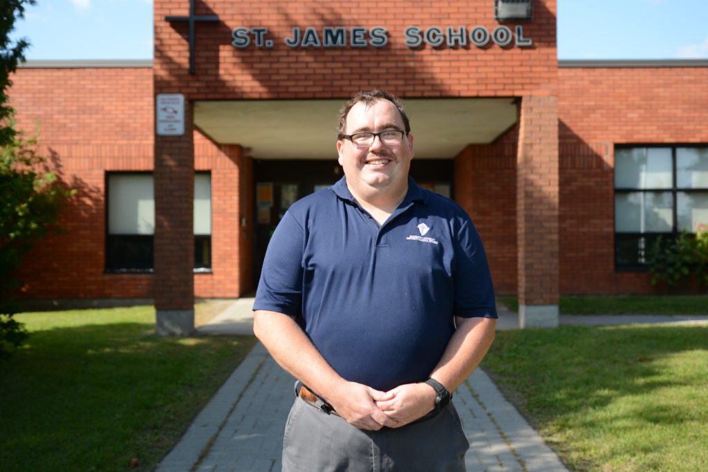 Custodian stands in front of a school outside.